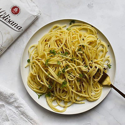Plate of spaghetti with a fork on a light surface, featuring a branded napkin.