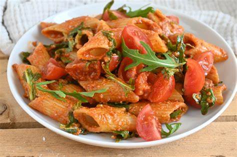 Penne pasta with tomatoes and arugula on a white plate