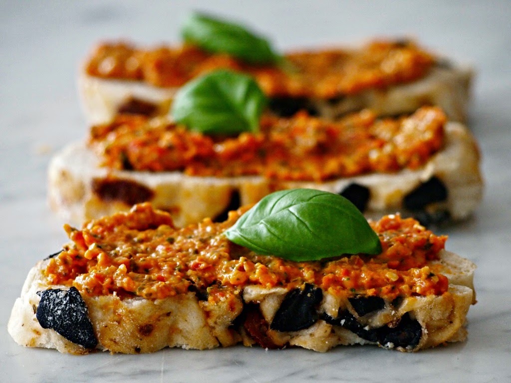 Bruschetta with tomato pesto, olives, and basil leaves on a marble surface.