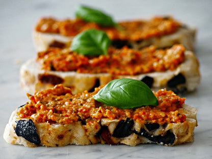 Bruschetta with tomato pesto, olives, and basil leaves on a marble surface.