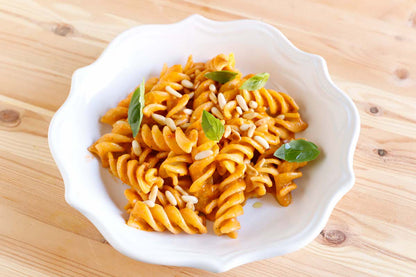 White bowl of orange pasta with green leaves on a wooden surface