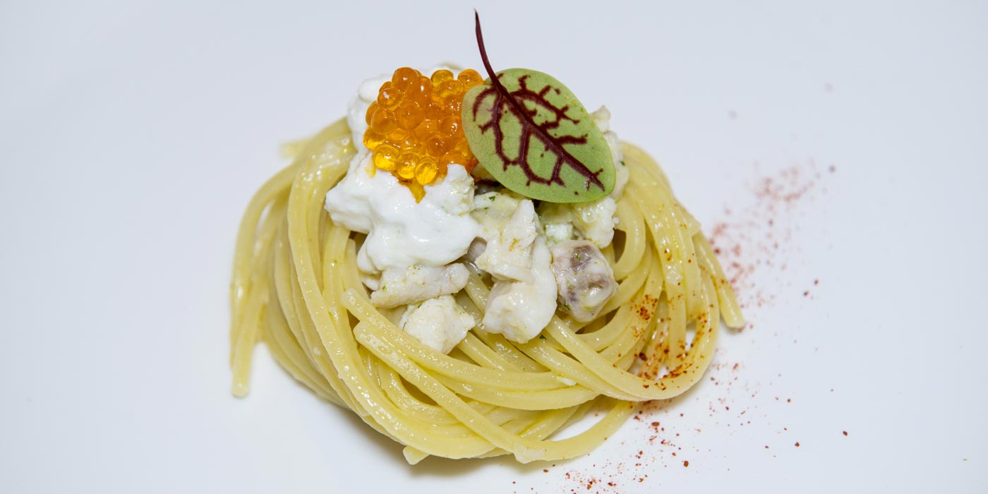 Pasta dish with crumbled white cheese, orange caviar, and a leaf on a white background