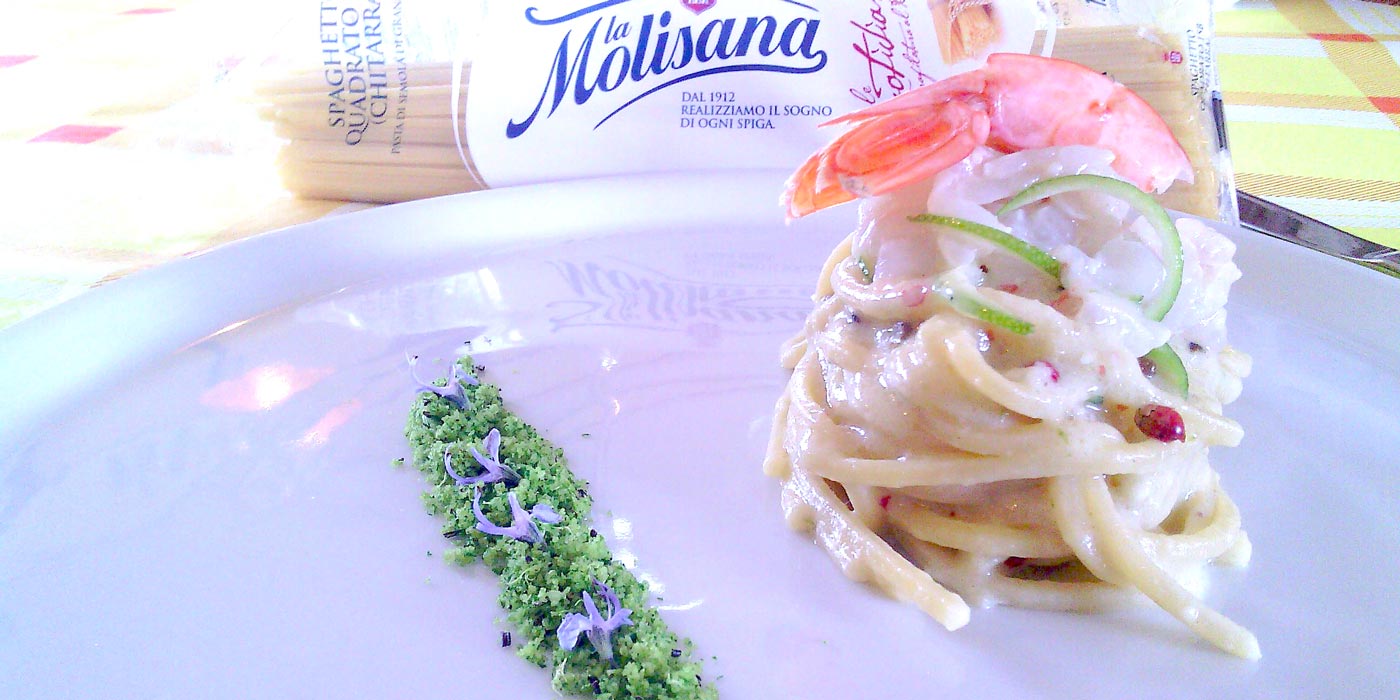 Pasta dish with seafood and vegetables on a white plate, featuring Molisana pasta packaging.